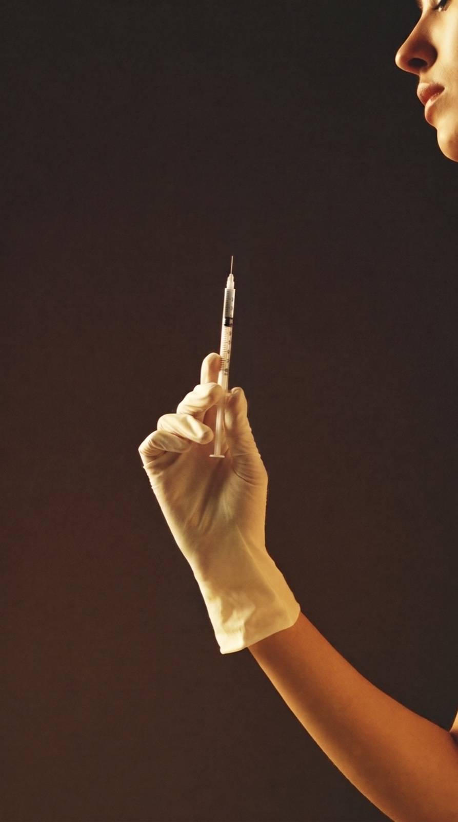 A gloved hand holding a fine cosmetic syringe in warm, refined light
